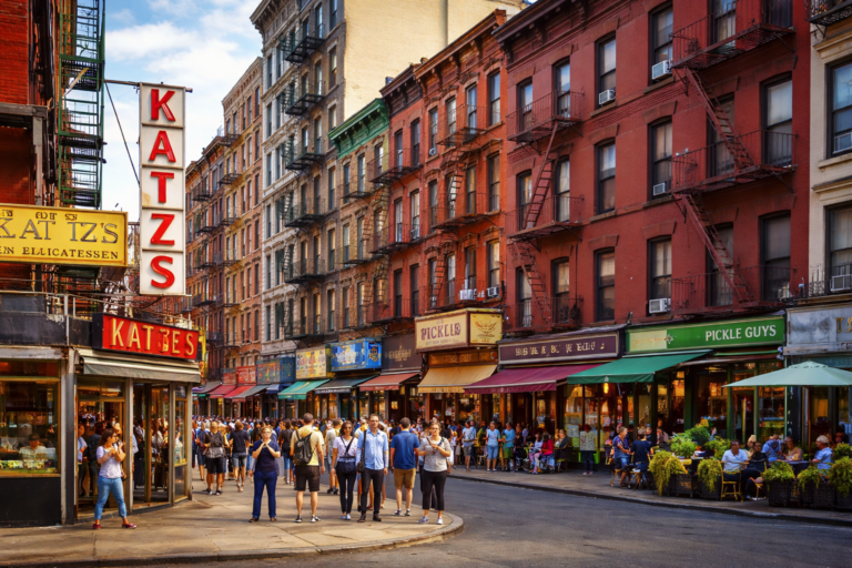 Lower East Side NYC street scene with historic tenement buildings, fire escapes, busy sidewalks, and Katz’s Delicatessen sign